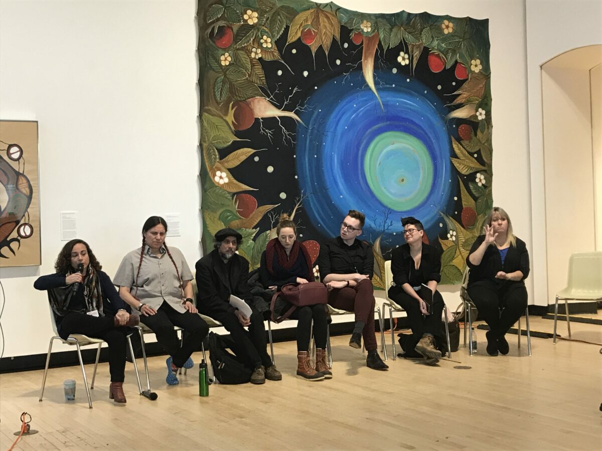 A row of people in chairs in front of a large painting.