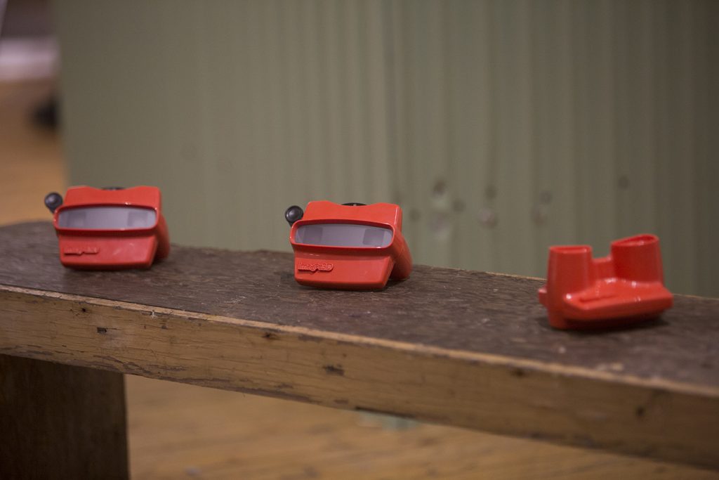 Three red stereoscopes on a wooden bench.