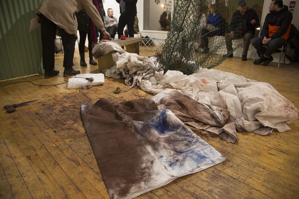A gallery installation with dirty white sheets and green chain-link fencing.