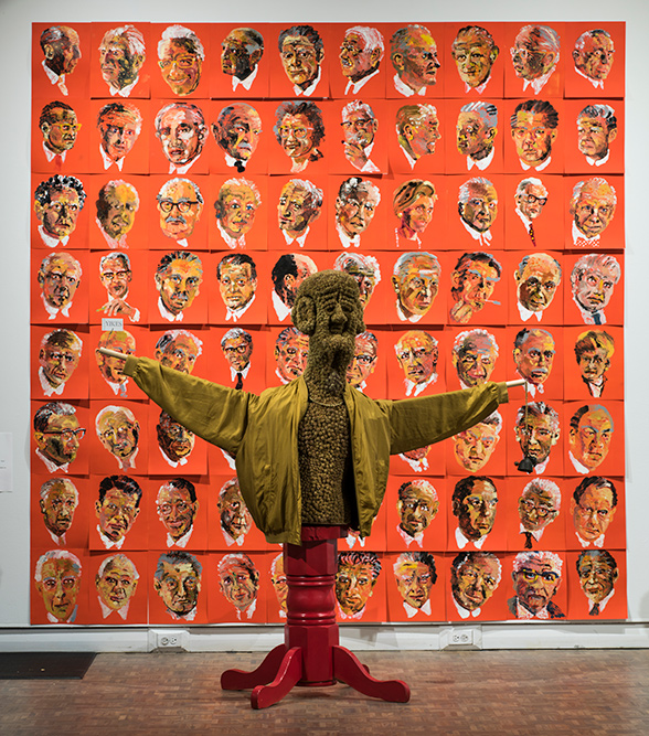 A burdock scarecrow in front of a wall of portraits.