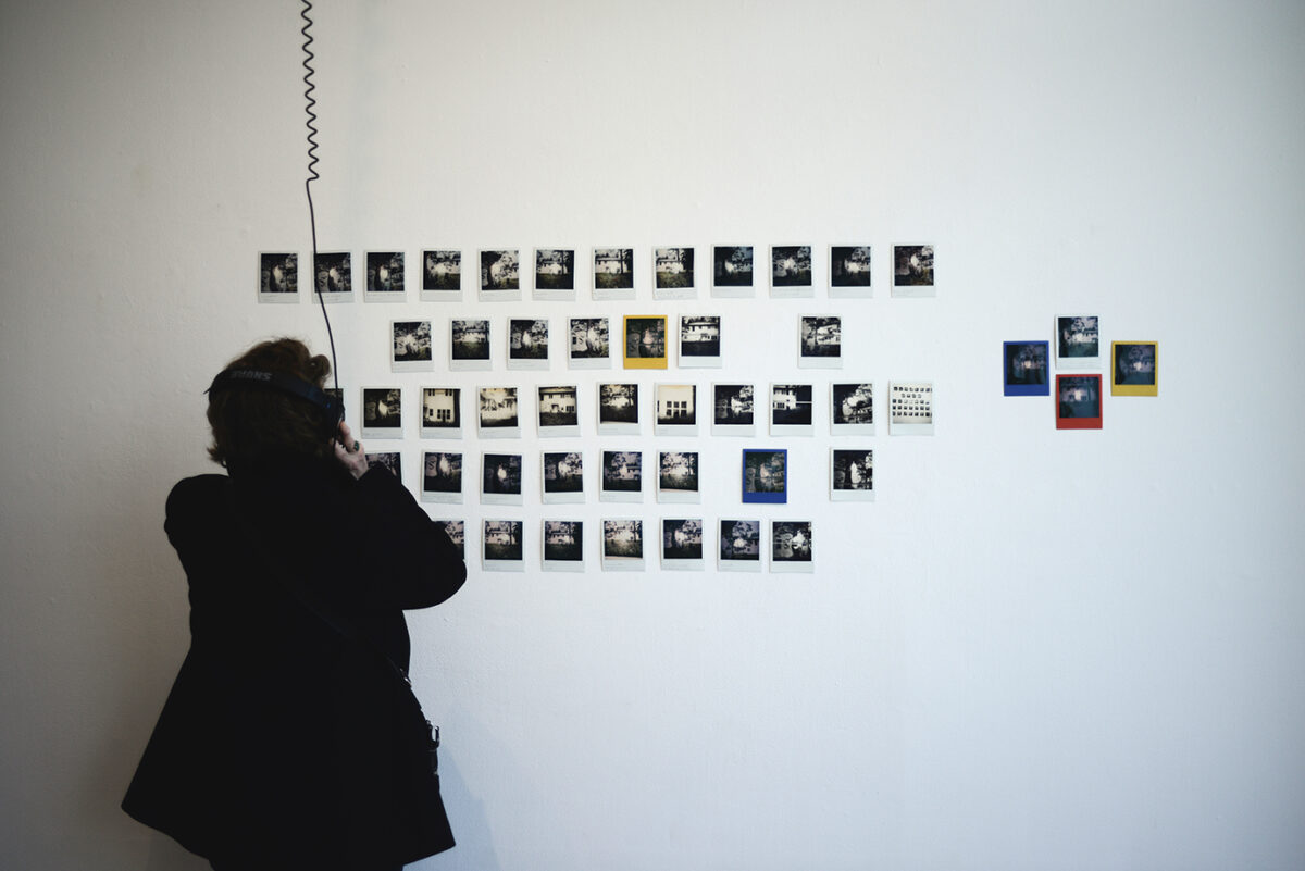 A gallery visitor looking at a wall of polaroid photos.