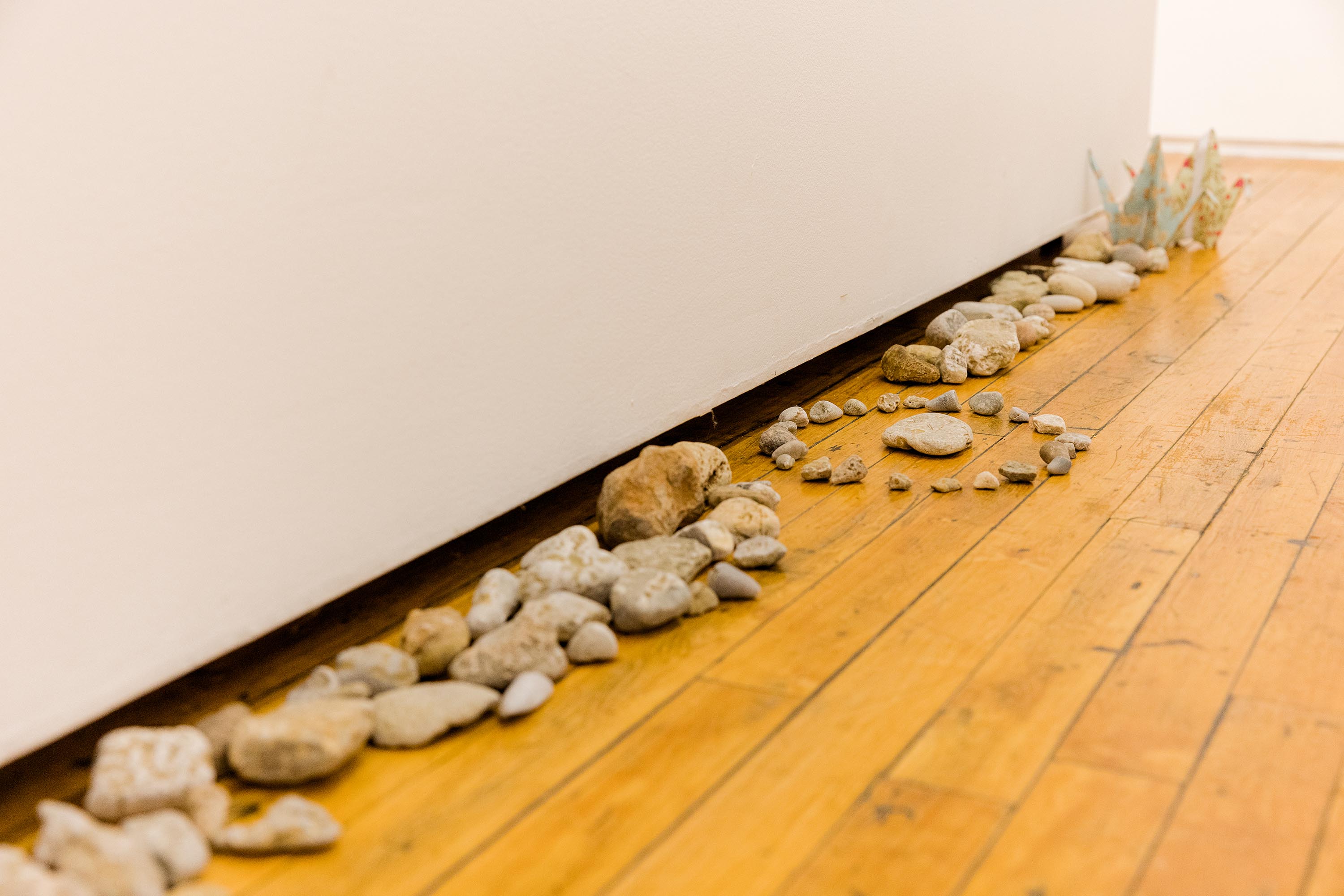 Many small stones arranged against a gallery wall. A ring of stones sits in the middle.