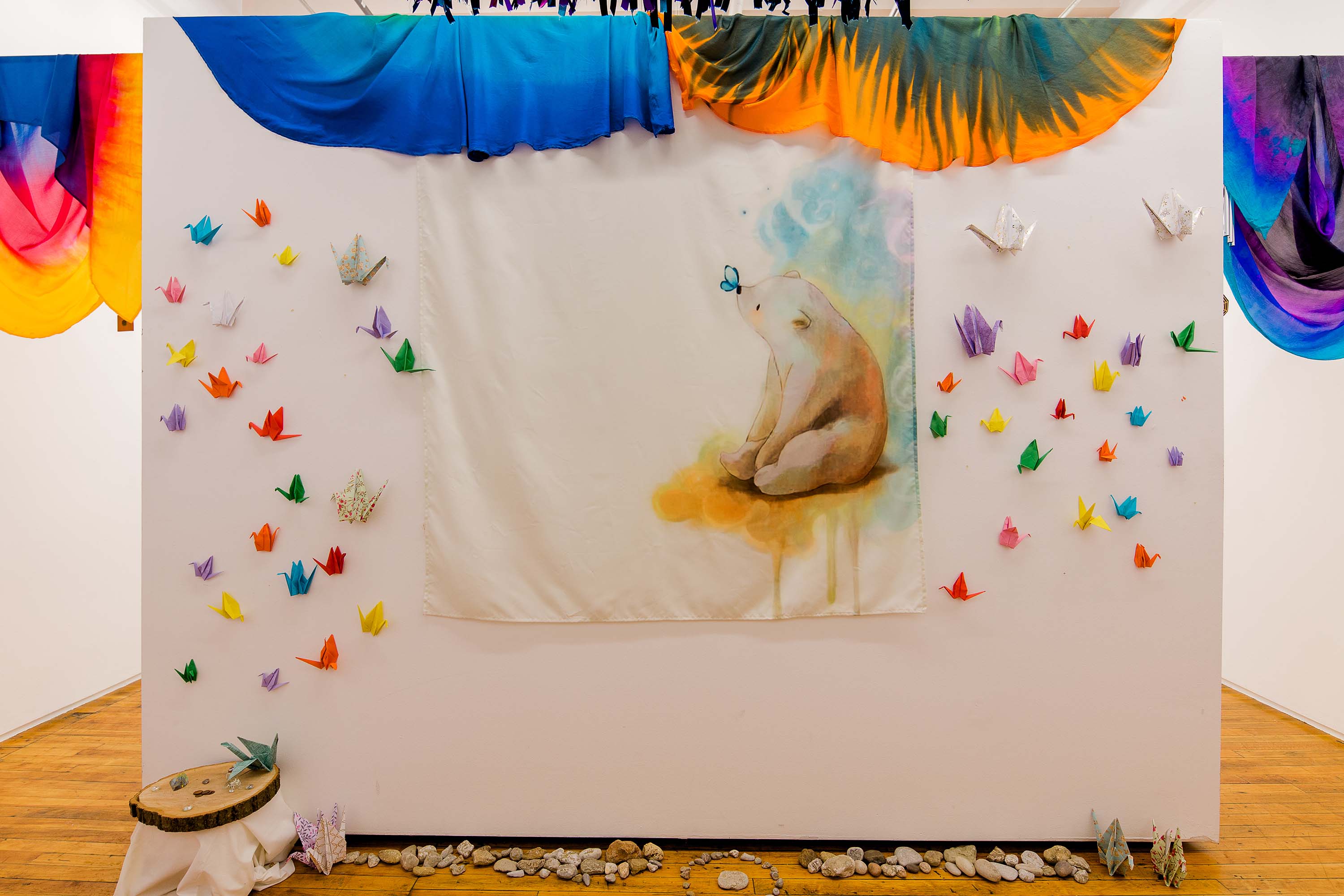 A white screen draped with scarves and hung with paper cranes and a tapestry.
