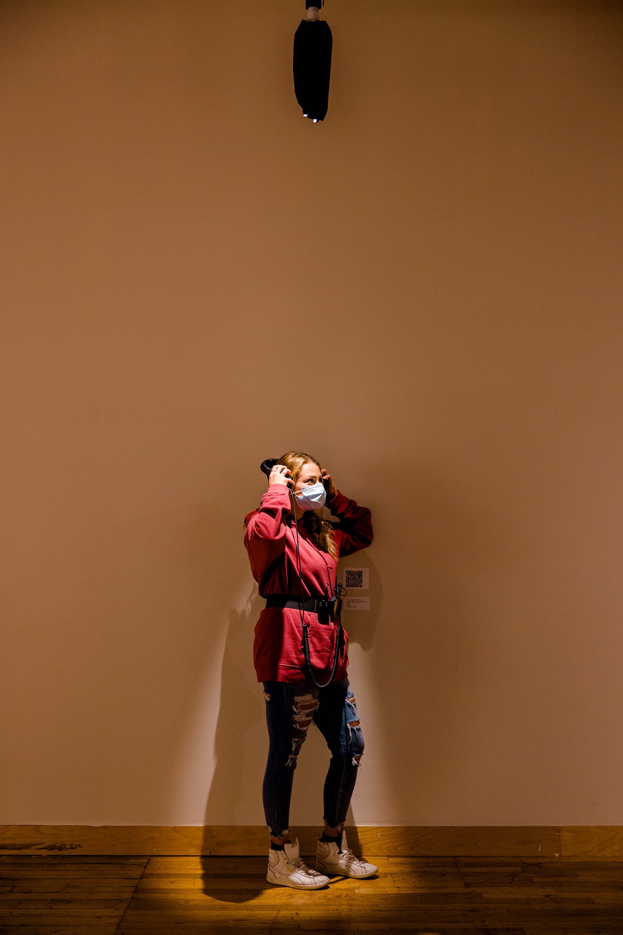 A person wearing headphones standing in front of a gallery wall.