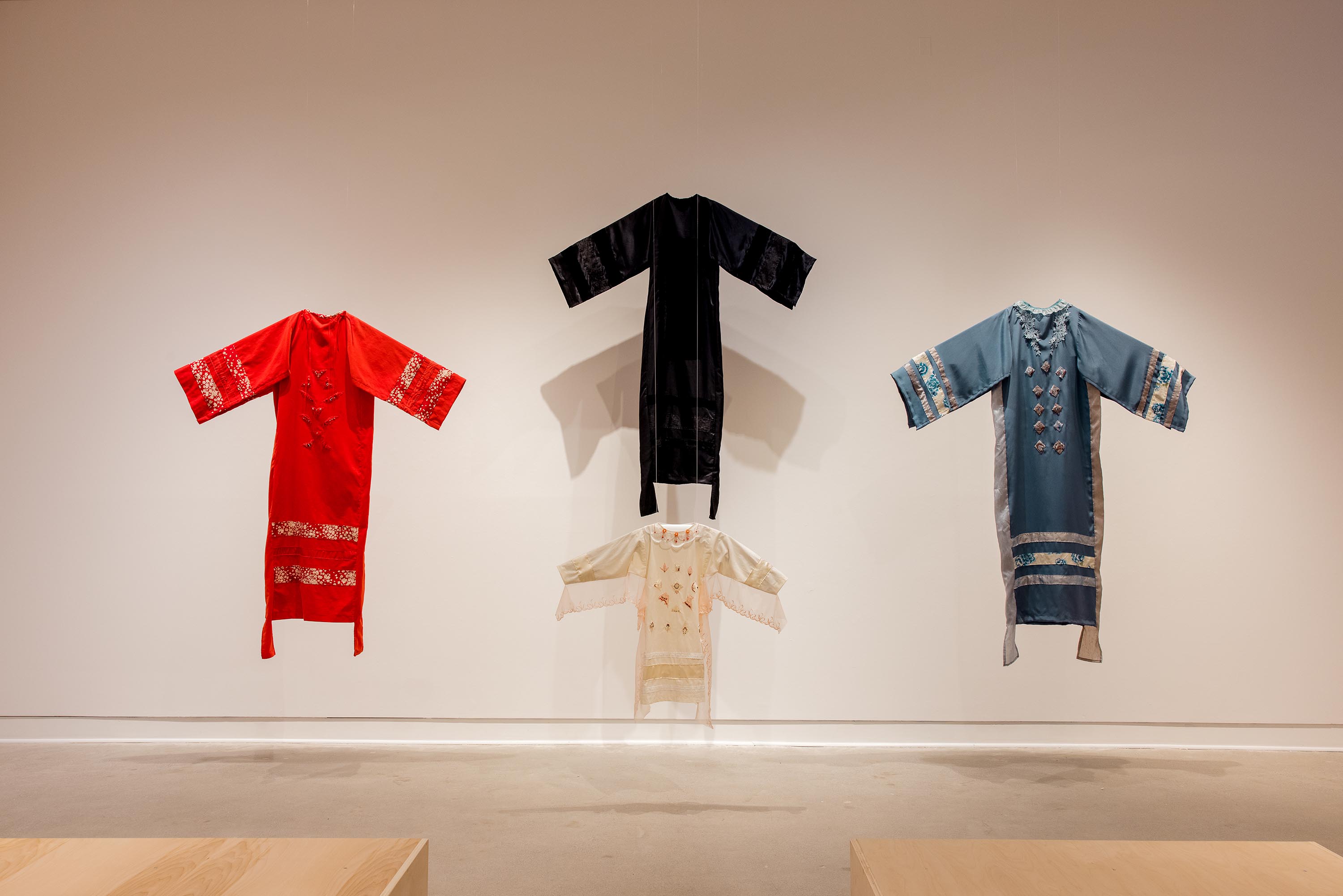 Four long beaded dresses hanging in a gallery.