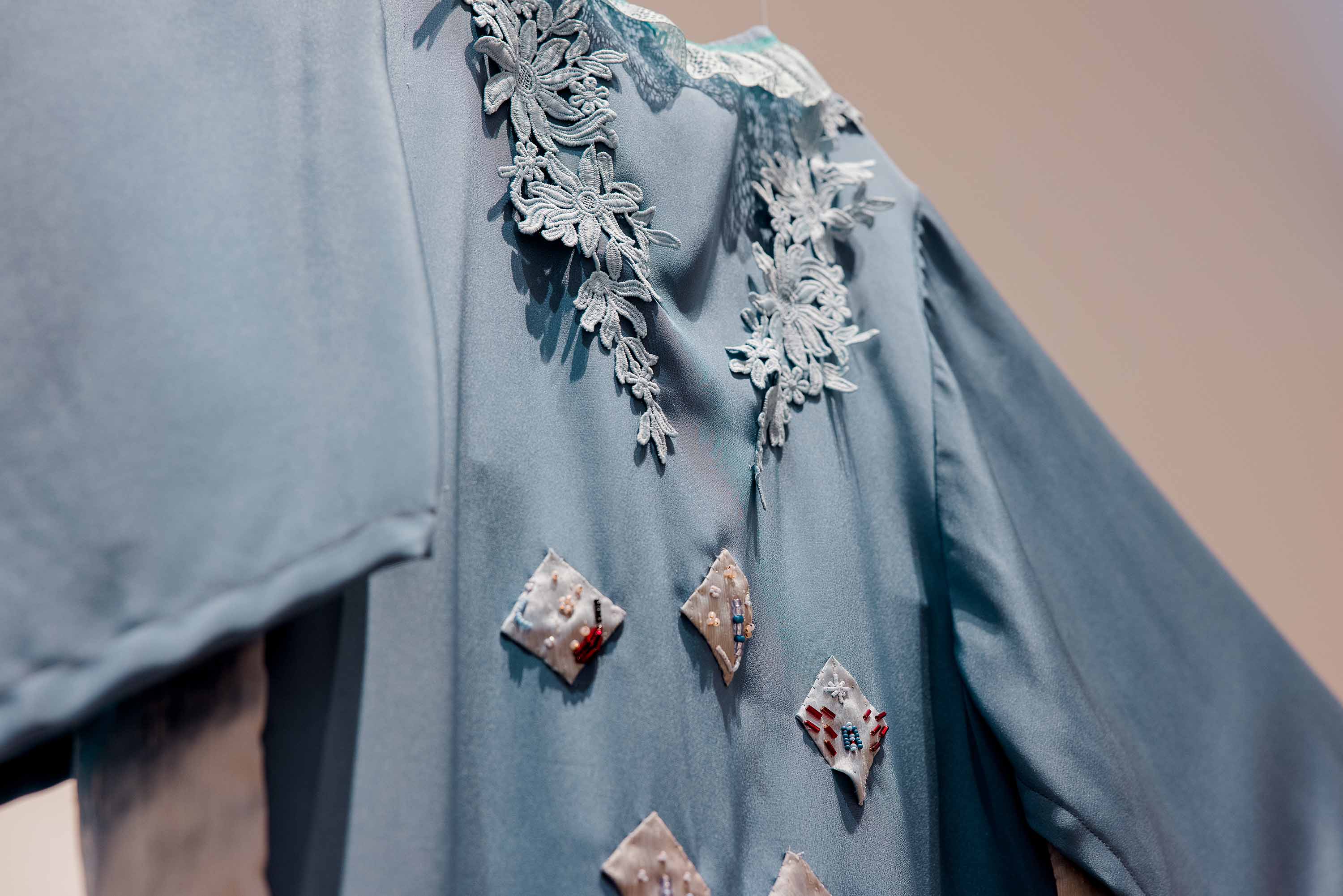 A close-up of a blue dress with lace trim and beaded appliques.
