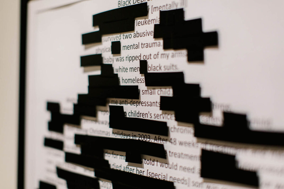 A close-up of a canvas printed with black text. Some of the words are covered with squares of black paper.