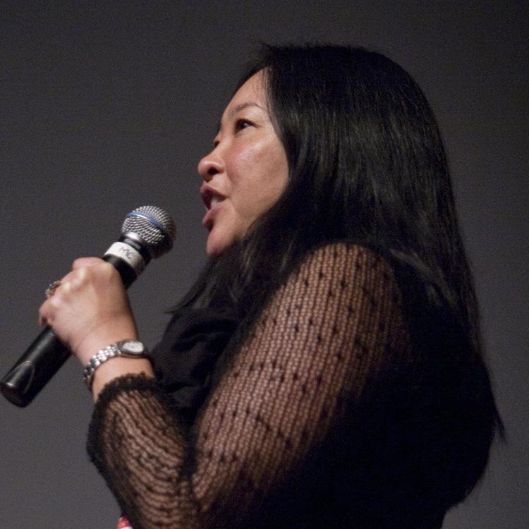 Holding a microphone, Nadine delights in answering a question at ReFrame Film Festival in Peterborough 2015 about the growing archive of Re•Vision multimedia digital stories. Her hair is long and black, and she is now proudly growing-in the platinum, so this photo will soon change.