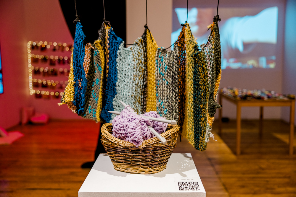 A knitted hammock-like installation and a basket holding a piece of purple knitting.