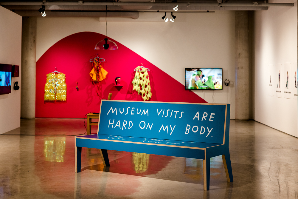 A blue bench with text reading, museum visits are hard on my body.